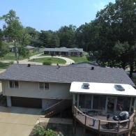 Overhead view of a two-story beige house with a gray roof and a screened-in porch with a wooden deck.