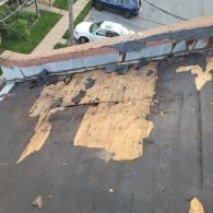 Damaged roof with exposed wood and missing shingles, cars and a sidewalk are in the background.