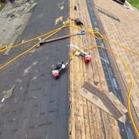 Roofing work in progress; two pneumatic nailers, one crowbar, yellow air hoses, and partially stripped roof.