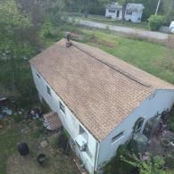 Overhead view of a house with a brown shingle roof, surrounded by grass and trees.