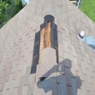 Damaged roof with missing shingles exposing wooden structure. Brown shingles, gray wood, shadow of a person.