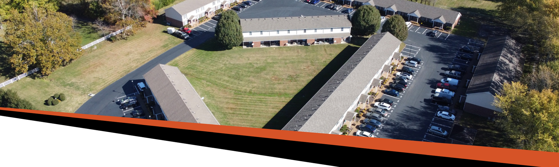 Aerial view of a building complex with a grassy courtyard and parking areas, surrounded by trees.