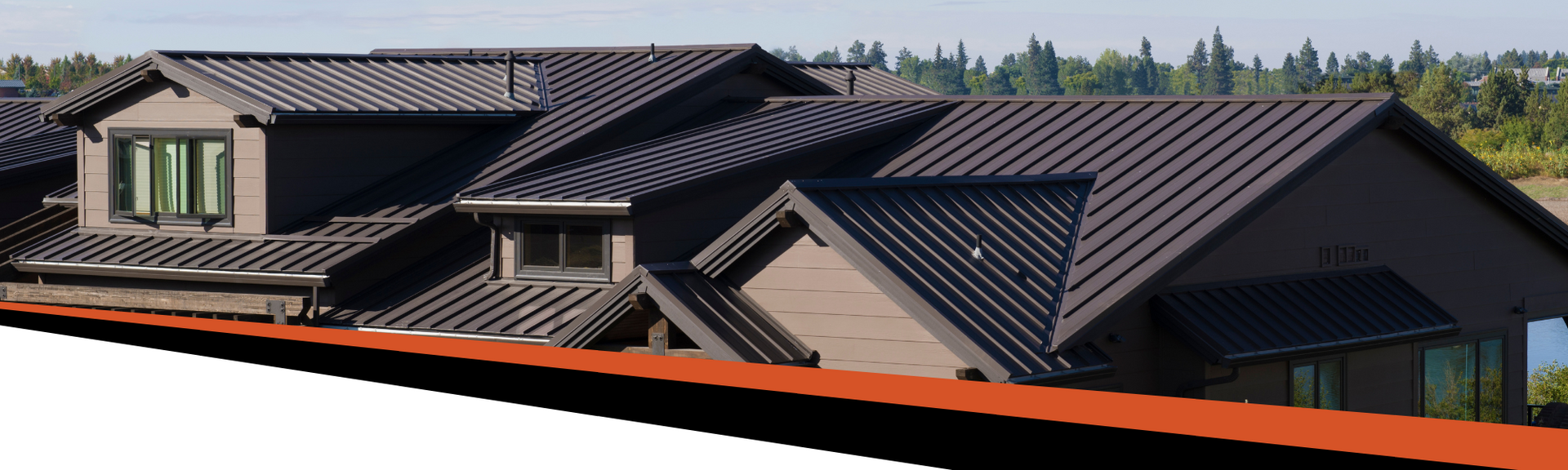 A dark gray house with multiple gabled roofs, a red trim, and green trees in the background.