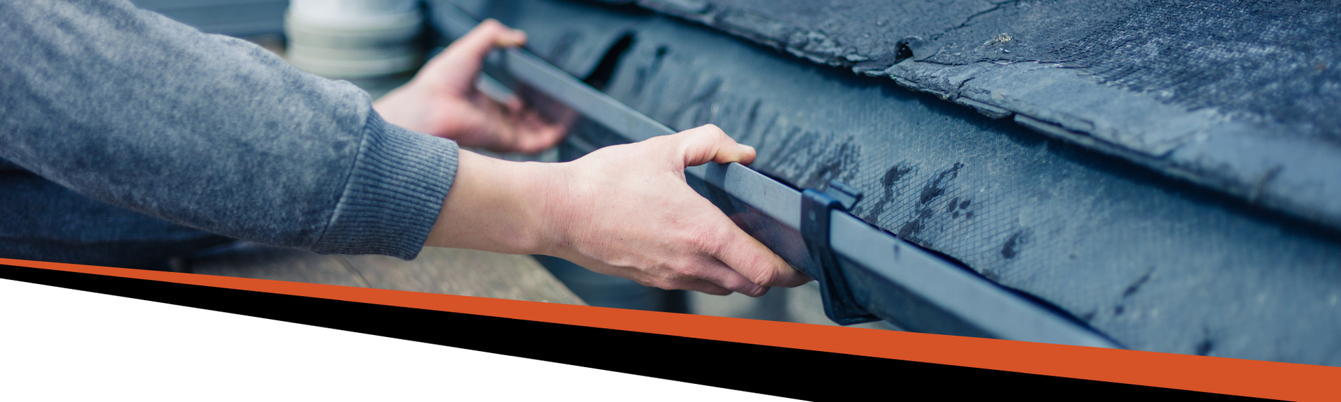 Person's hands holding a dark gray gutter, preparing to attach it to the roof.