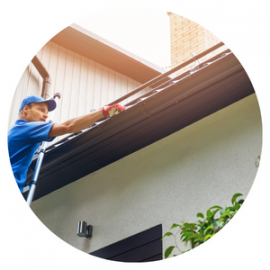 Person on a ladder cleaning a dark gutter on a white house.