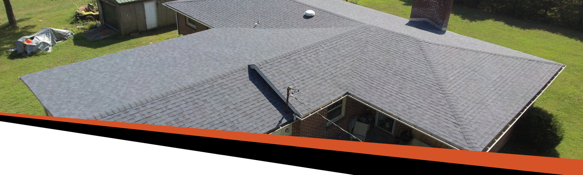 A house with a gray roof on a green lawn. There is an orange trim along the bottom of the image.