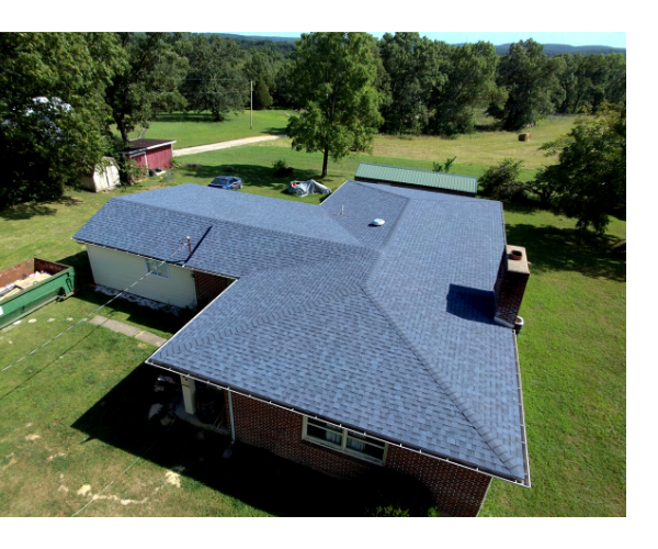 Aerial view of a house with a blue roof, surrounded by green grass and trees.