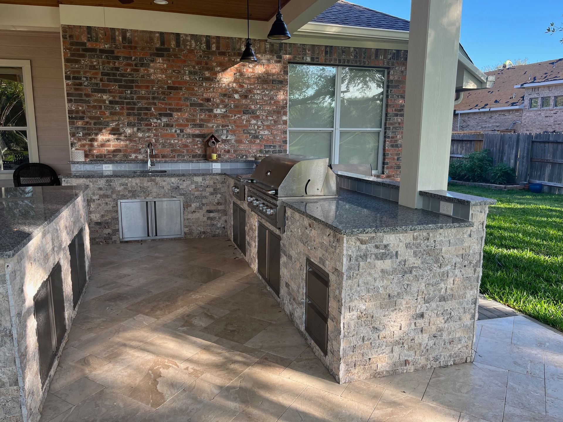 A large outdoor kitchen with a brick wall and granite counter tops.