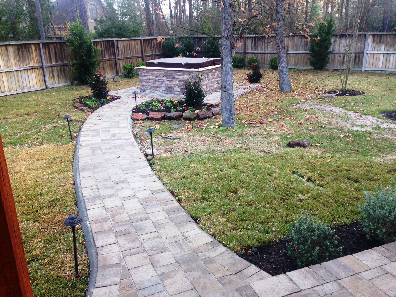 A brick walkway leading to a hot tub in a backyard.