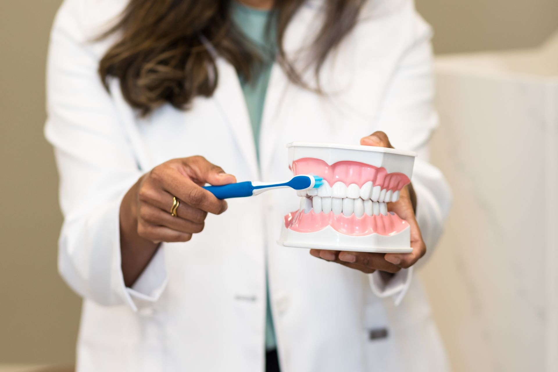 Dentist demonstrates brushing teeth with a model; blue toothbrush, white coat, focus on oral hygiene.