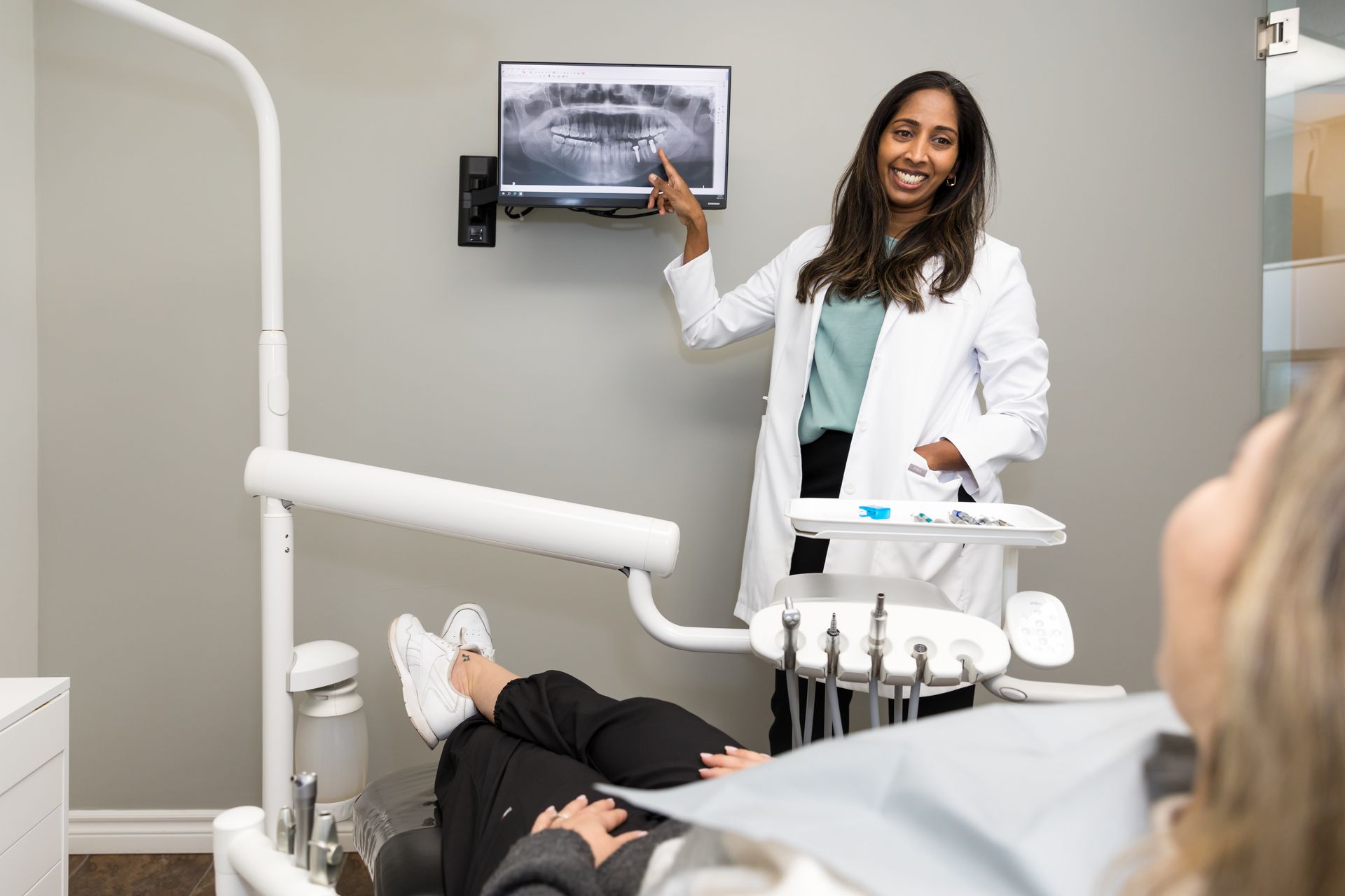 Dentist pointing at x-ray on screen, explaining to a patient in a dental chair.