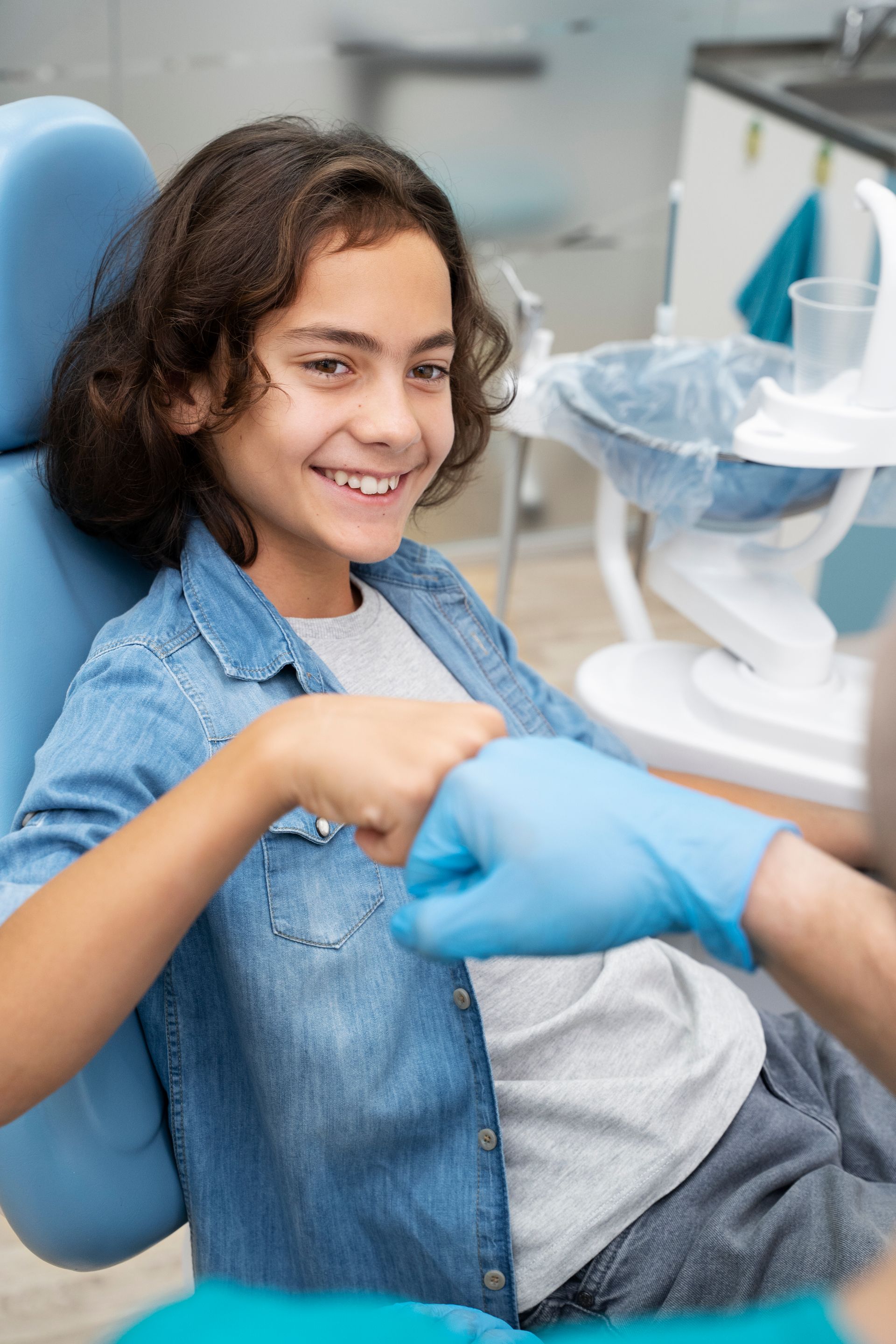 Boy smiles and fist bumps dental professional in blue gloves at dentist's office.