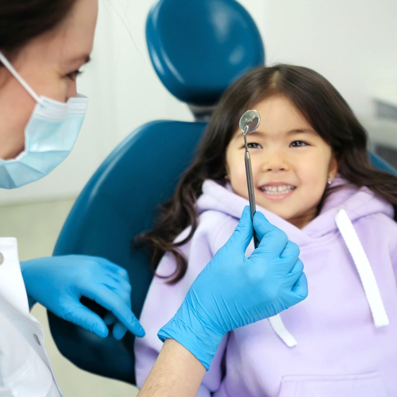 A dentist in blue gloves examines a young patient's teeth with a dental mirror in a dental office.