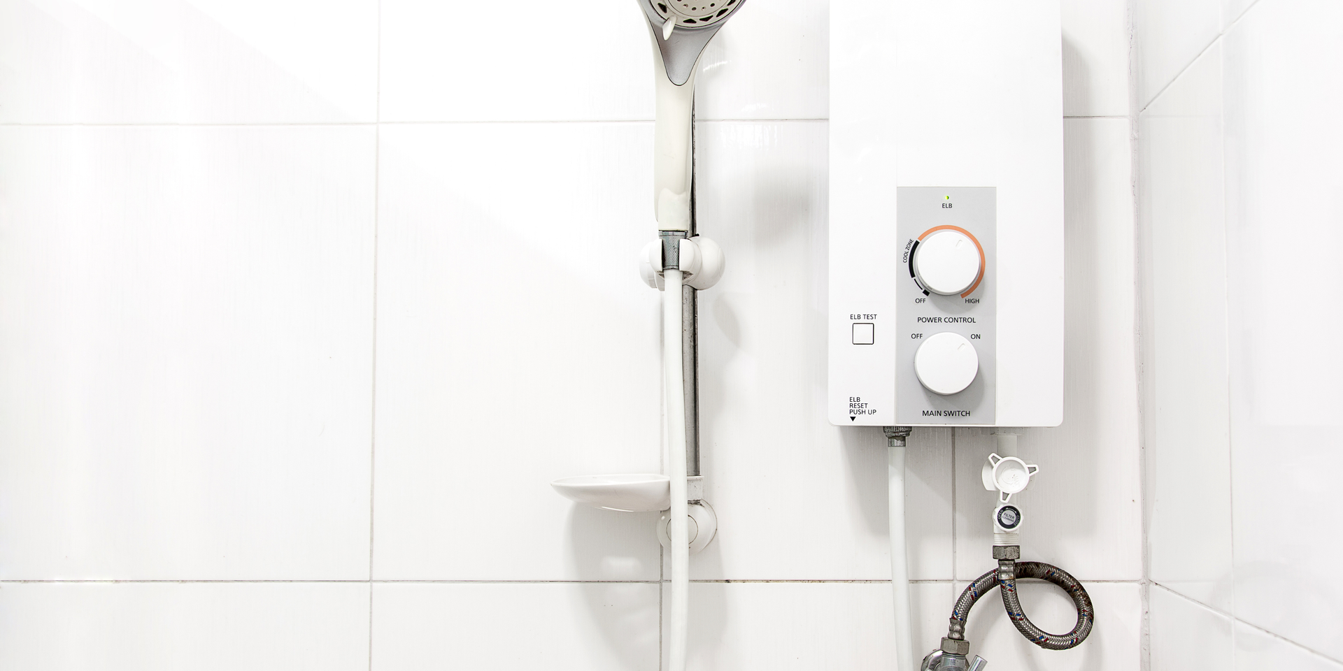 Shower with a white water heater, silver showerhead, and controls on a white tiled wall.