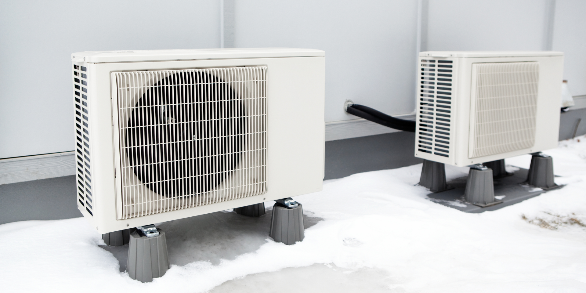 Two outdoor air conditioning units on a snowy surface.