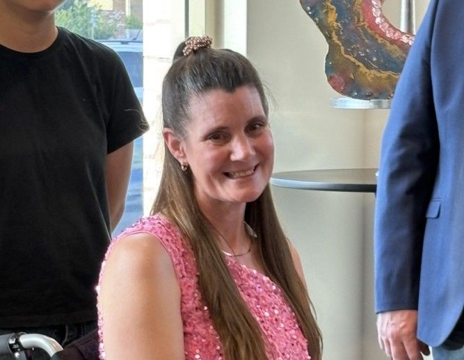 Dyan Moore, a first-time exhibiting artist in a wheelchair, smiles beside her colourful resin artworks at her exhibition.