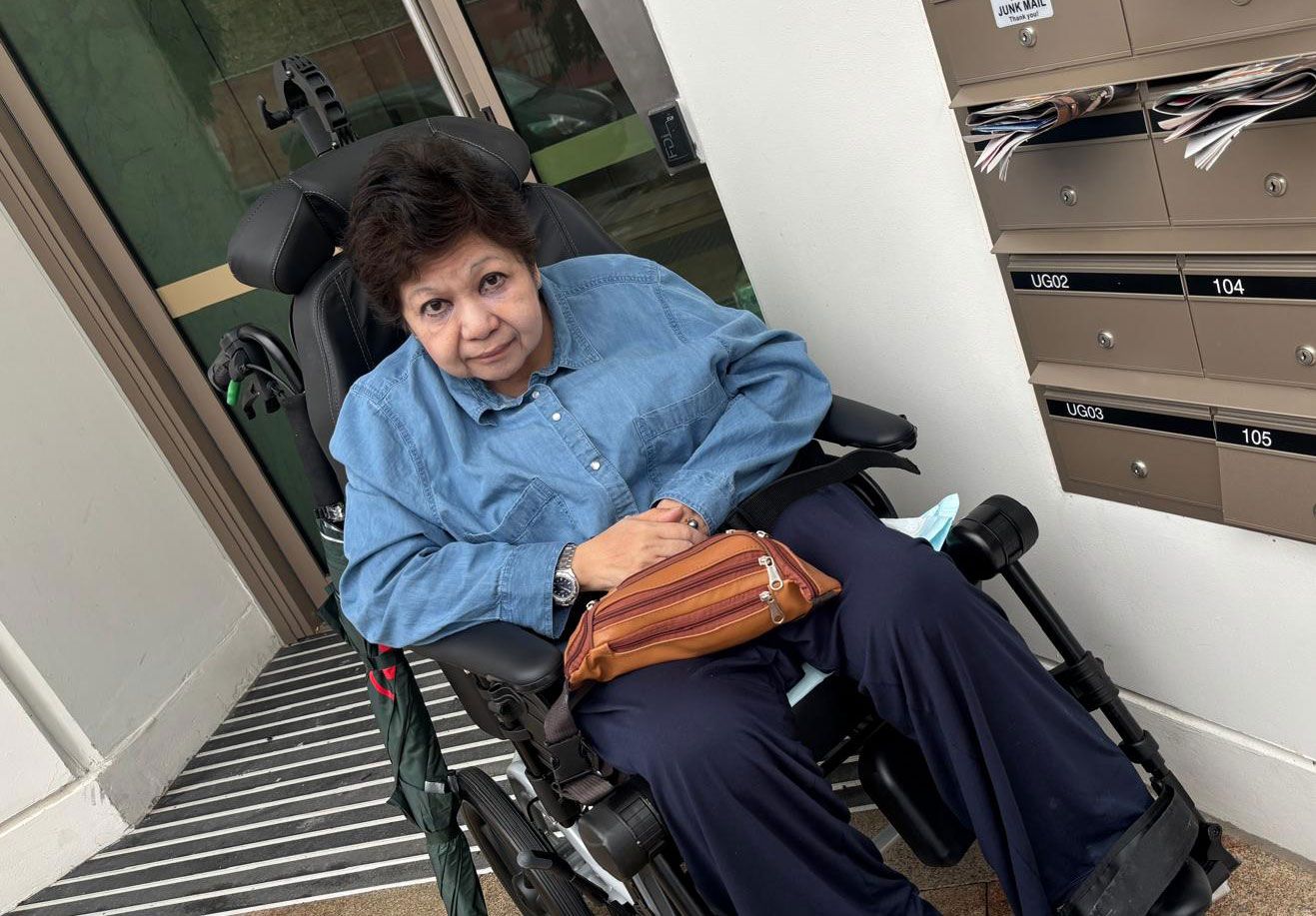 A woman is sitting in a wheelchair holding a purse in front of one of RQ Living homes.