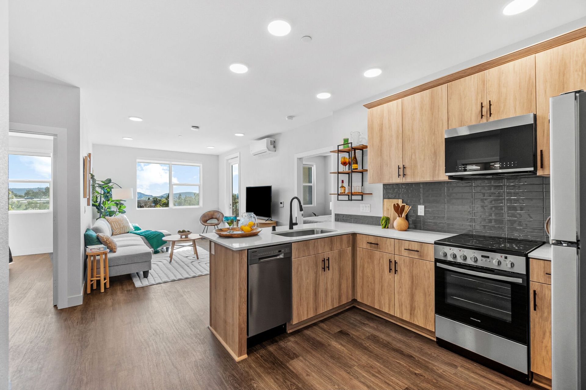 Open-concept kitchen and living area, with light wood cabinets, stainless steel appliances, and large windows.