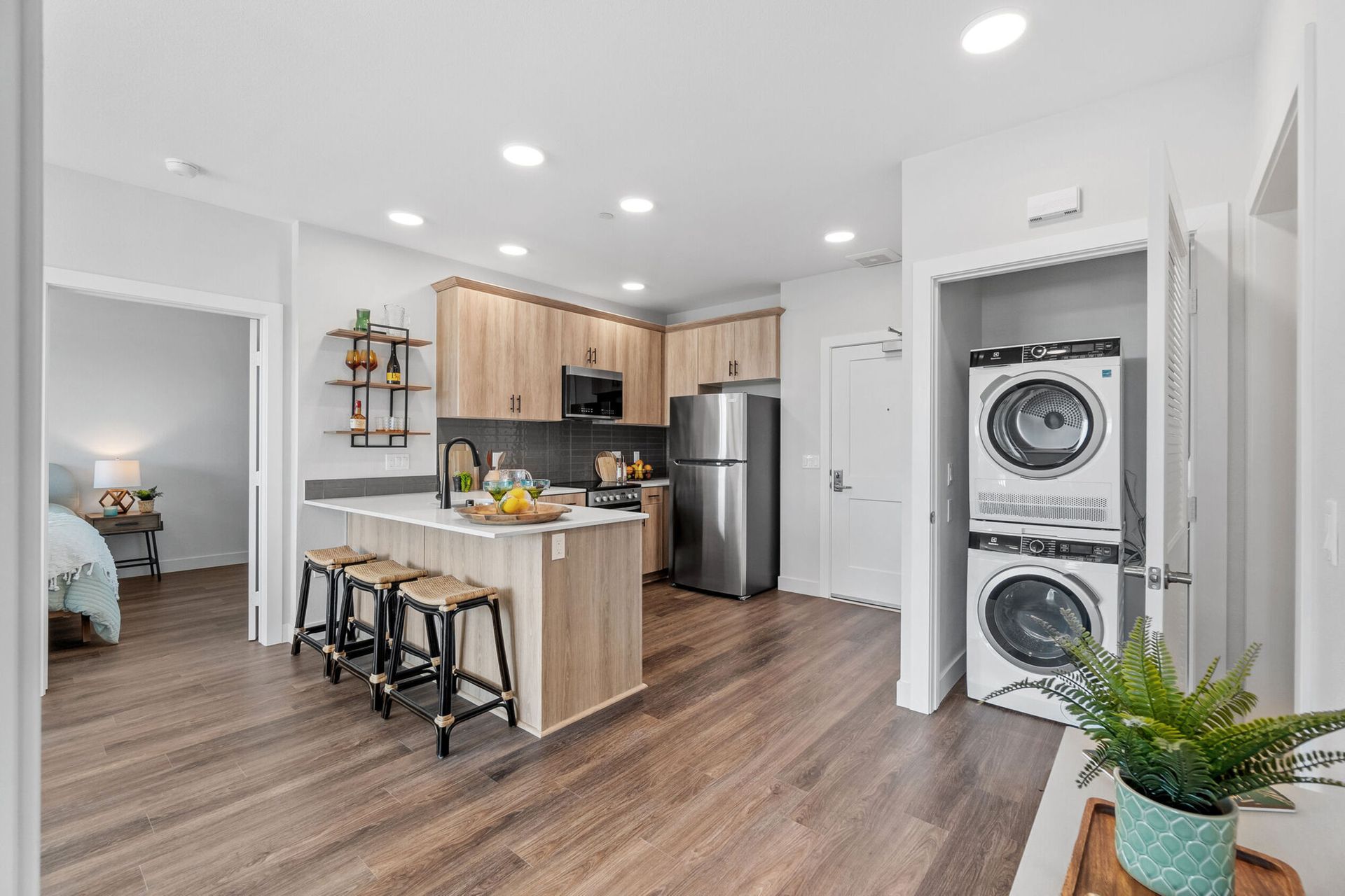 Open-concept kitchen and living area with island seating, stainless steel appliances, and stacked washer/dryer.