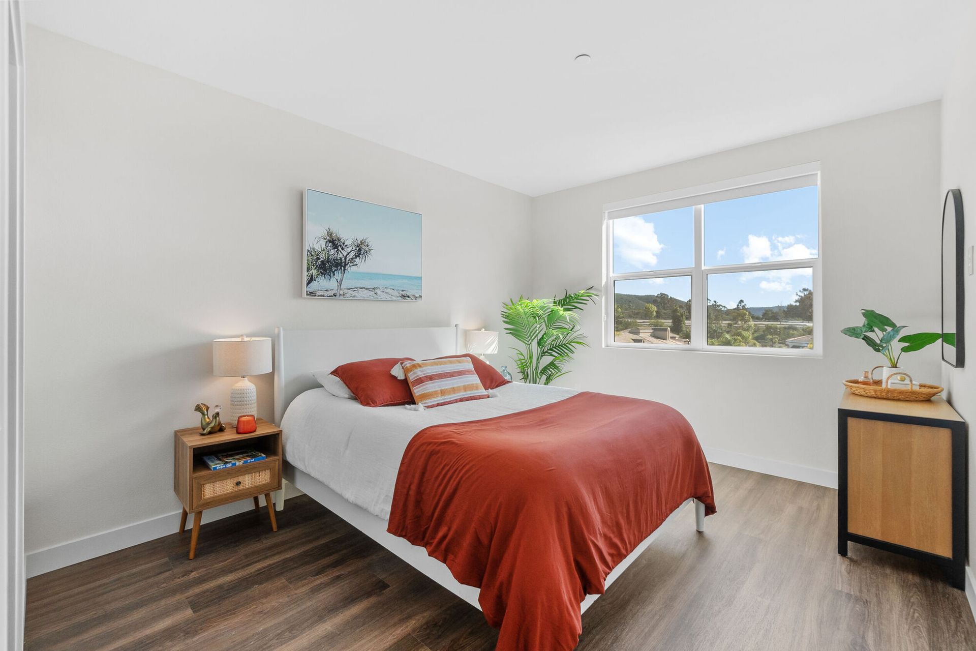 Bedroom with a white bed, rust-colored bedding, wooden nightstands, and a window with a view.