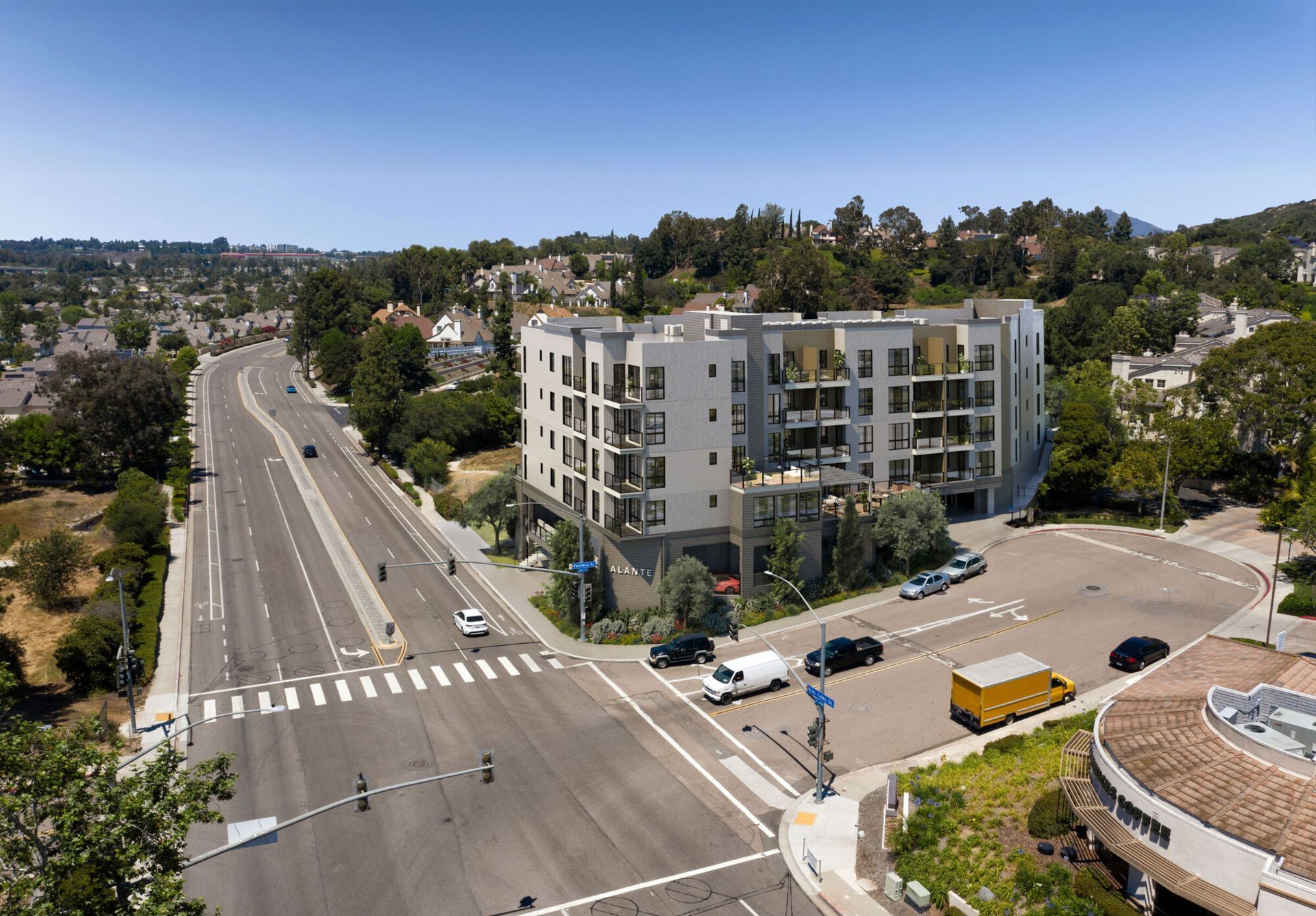Aerial view of a modern apartment building on a multi-lane road intersection under a blue sky.