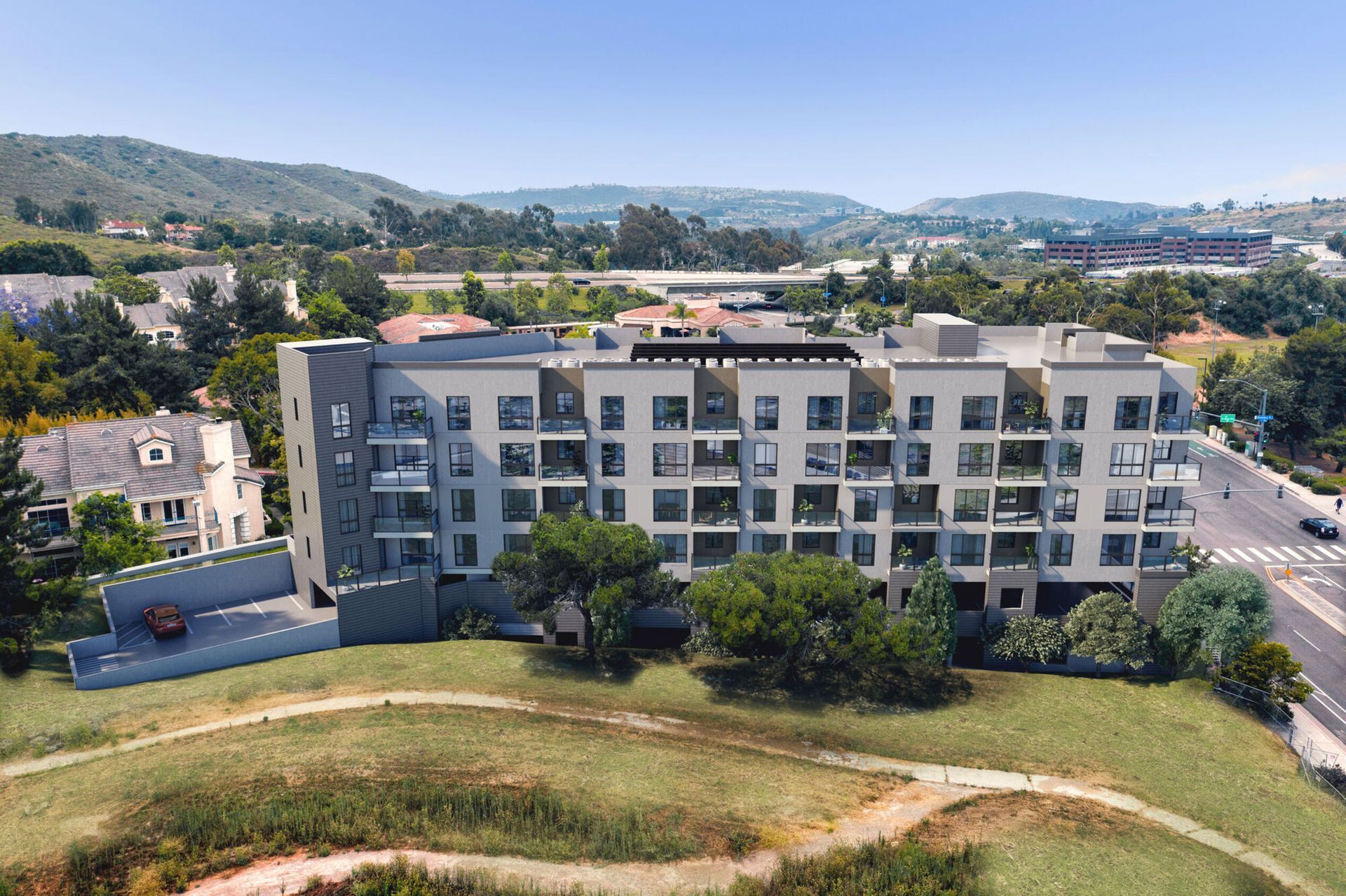 Multi-story apartment building with balconies, set against a green hillside and blue sky.