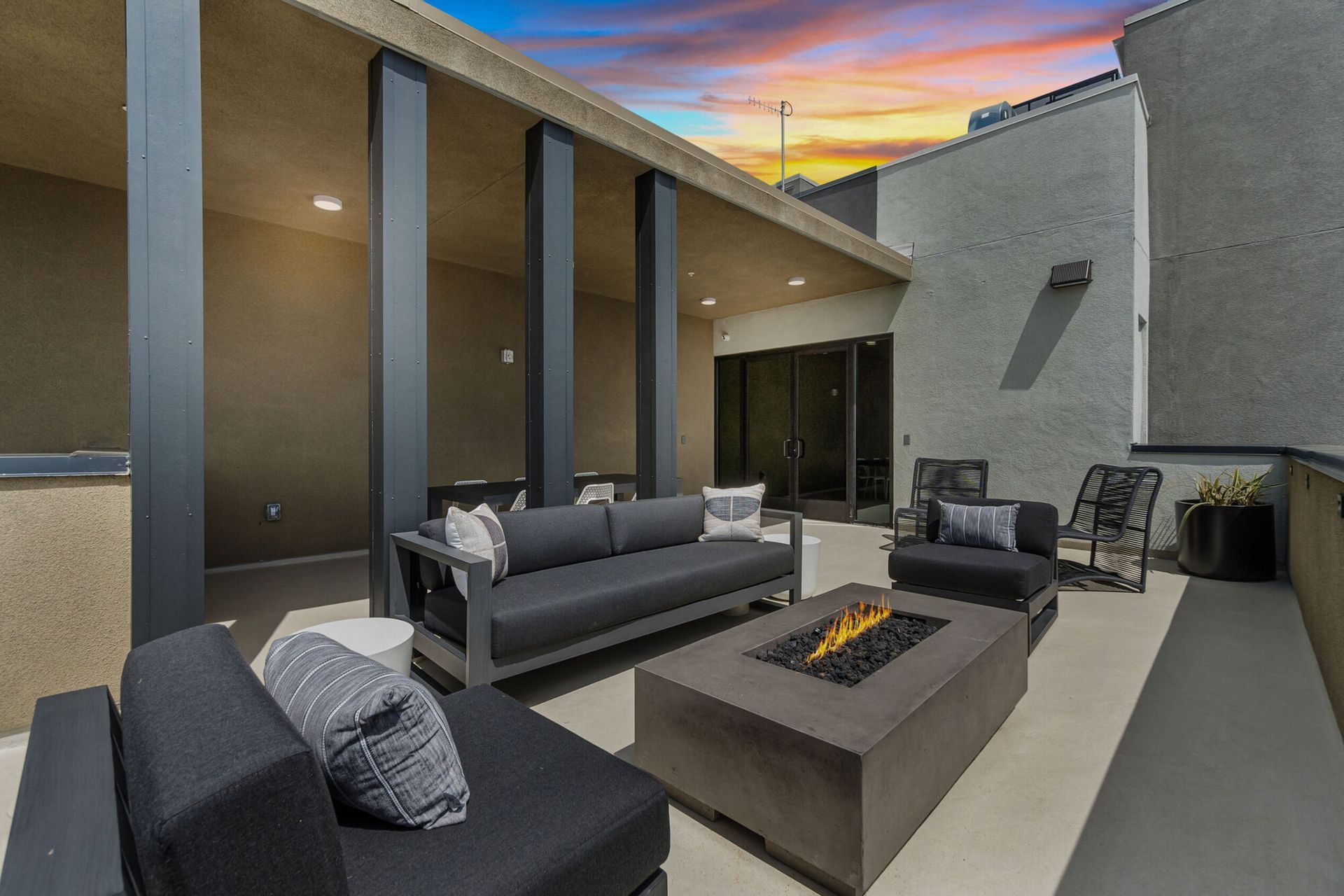 Patio with modern furniture, a fire pit, and a colorful sunset.