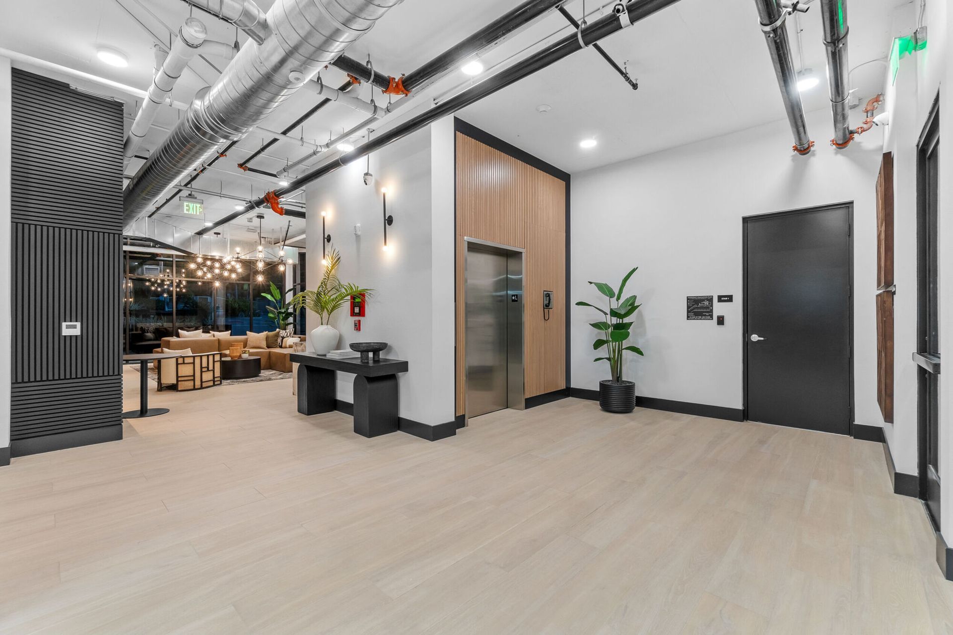 Modern lobby with light wood floors, an elevator, and a seating area in the background.