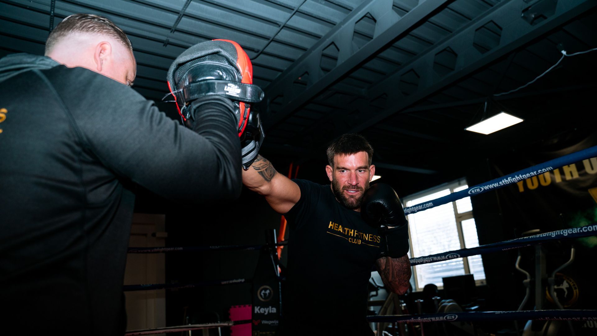 Twee mannen zijn aan het boksen in een boksring in een sportschool.