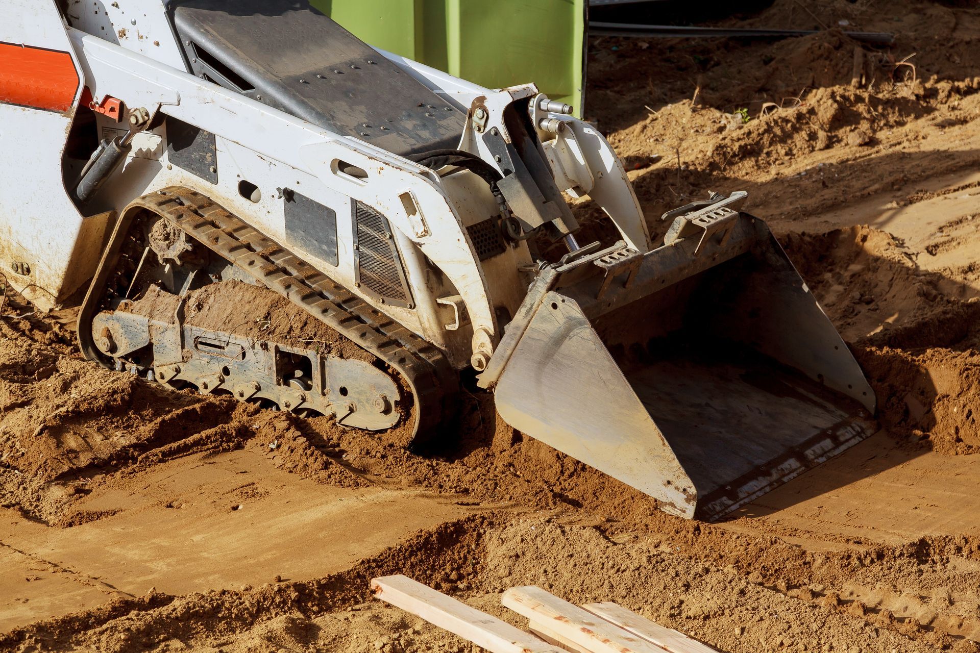 White skid-steer loader with a bucket scoop on sandy ground. White skid-steer loader with a bucket scoop on sandy ground.