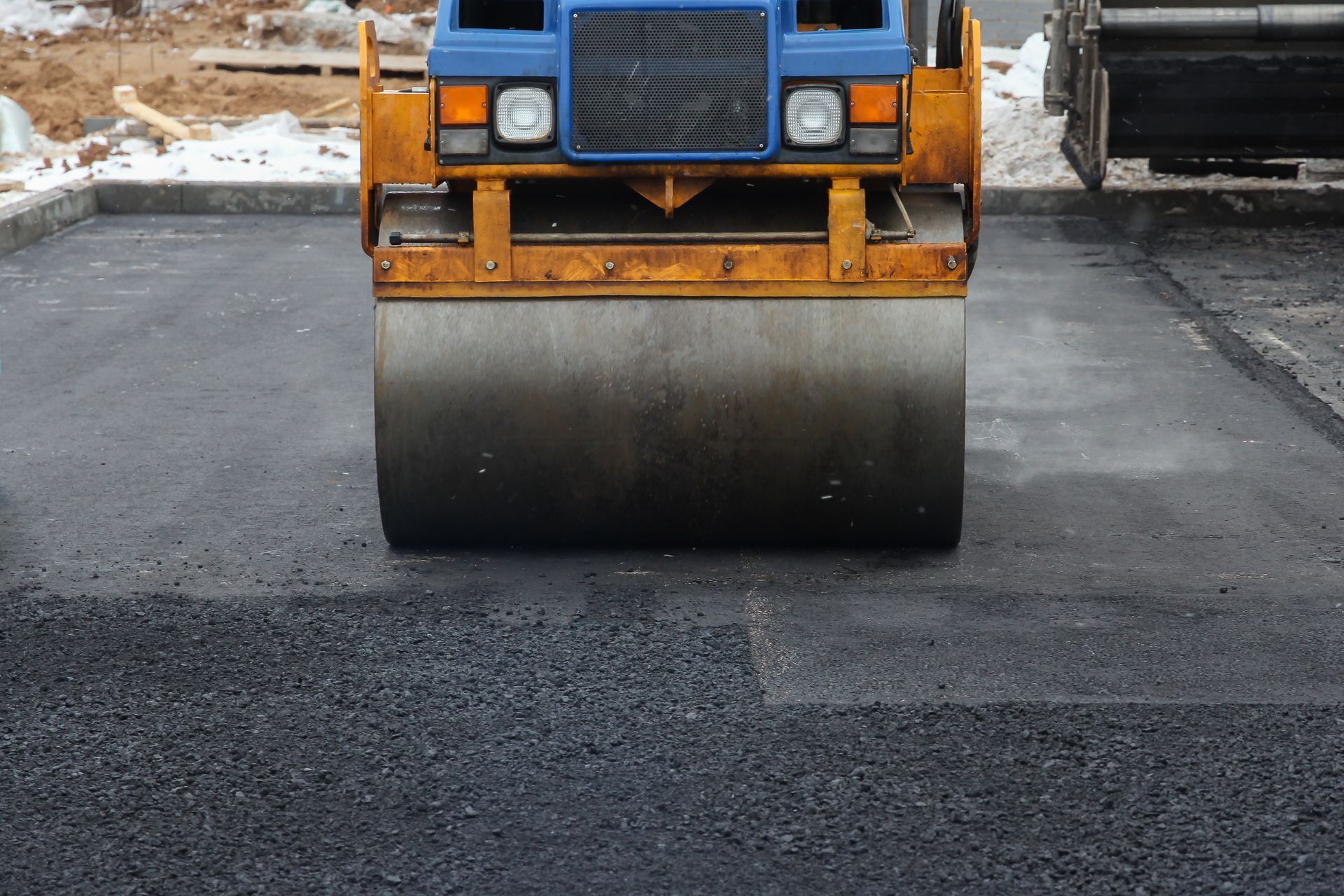 Road roller compacting fresh asphalt on a parking lot.