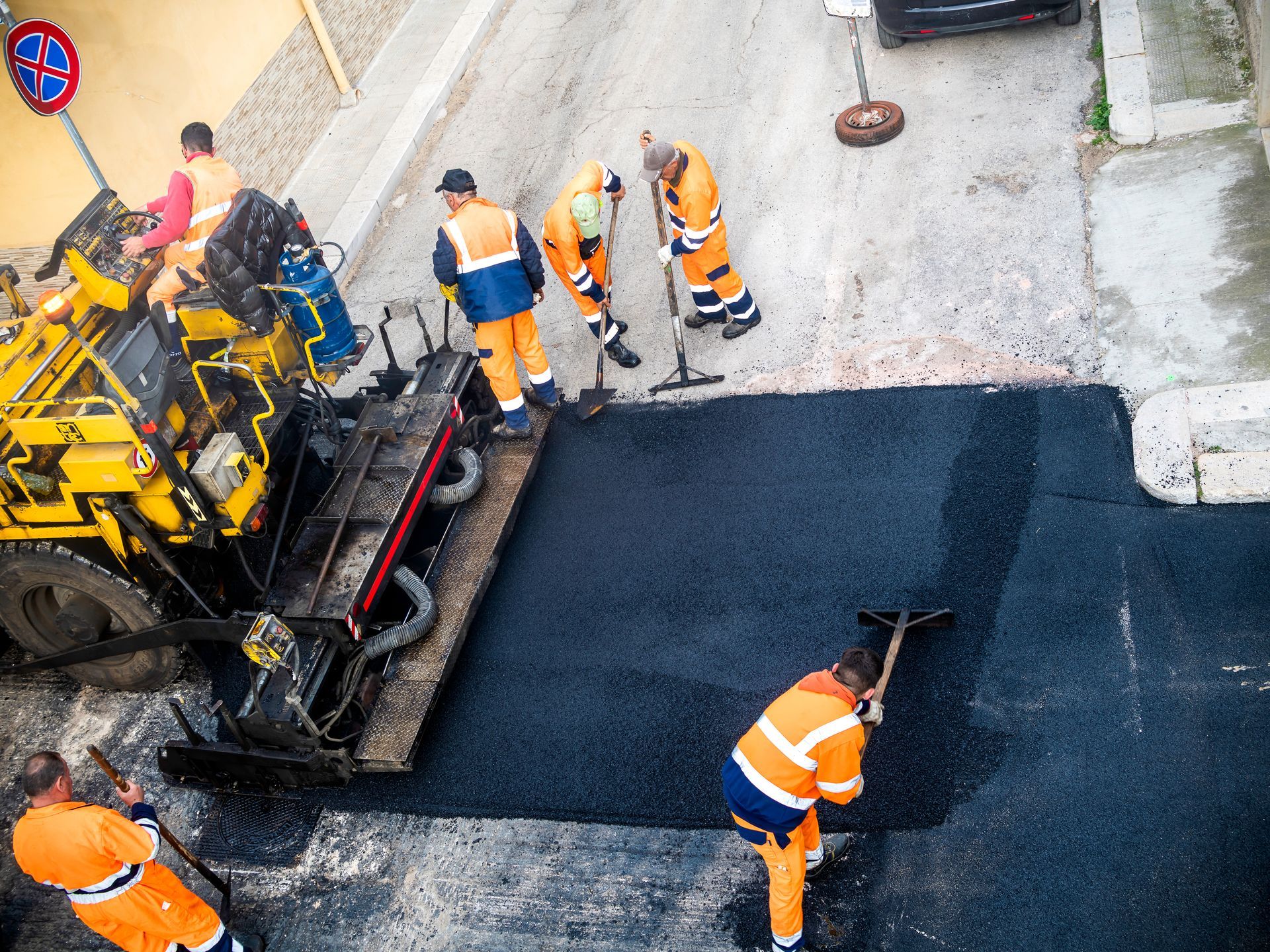 Road roller compacting asphalt on a newly paved road; blue sky in the background.