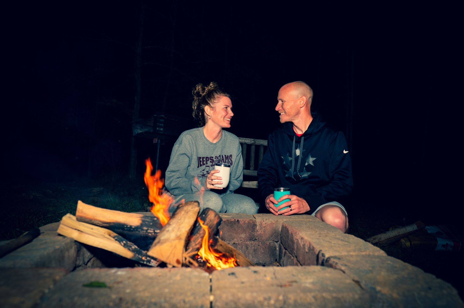 a man and a woman are sitting around a fire pit at night .