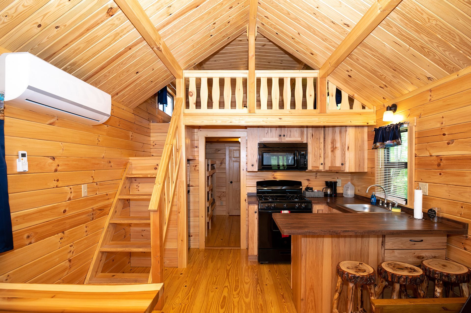 The inside of a small wooden cabin with a kitchen and stairs.