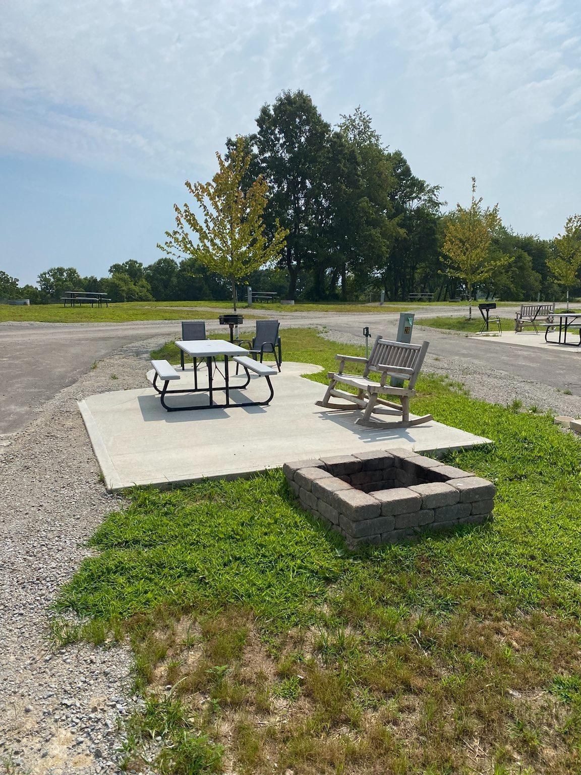 a picnic table and rocking chairs are sitting next to a fire pit .