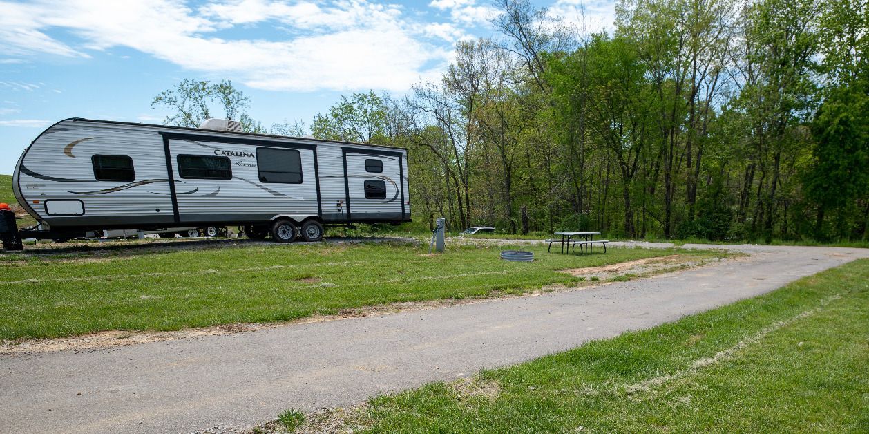 a rv is parked in a grassy field next to a path .