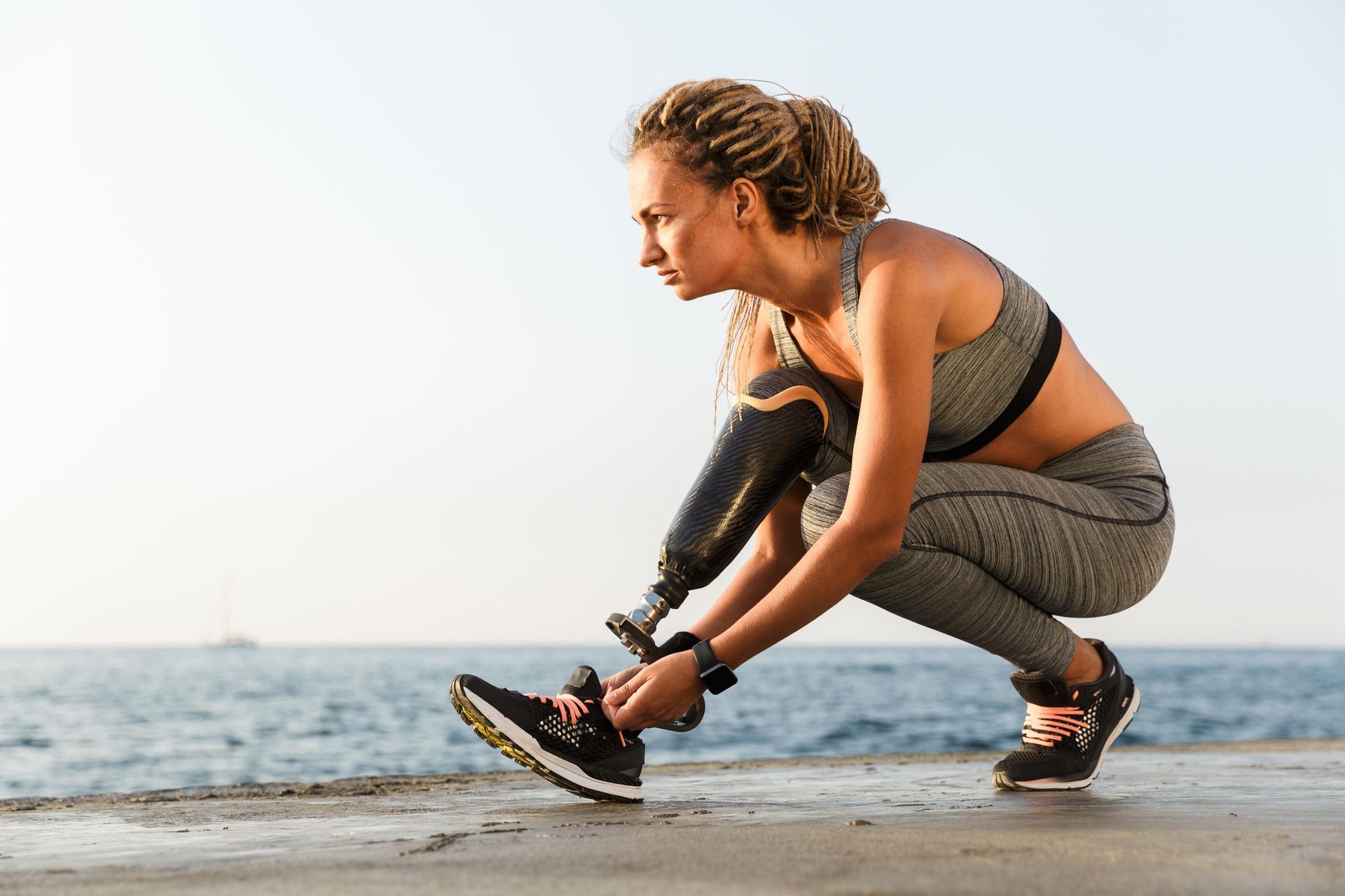 A woman with a prosthetic leg is tying her shoes on the beach.