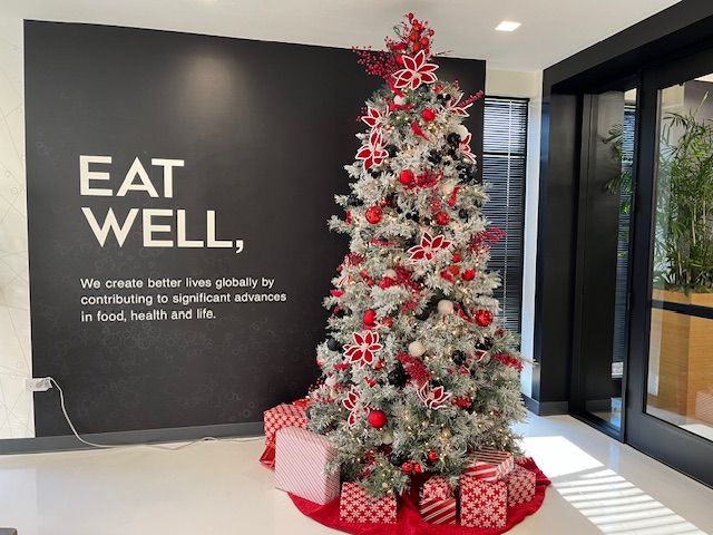 A decorated Christmas tree with red and white ornaments stands next to a black wall with the words