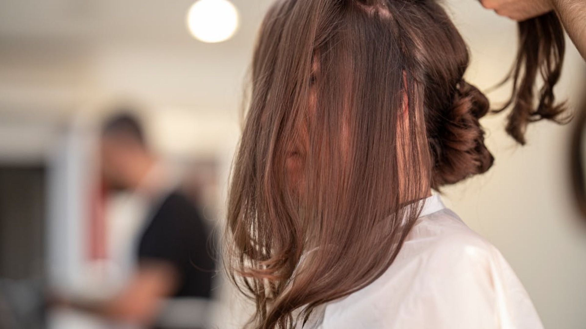 En una peluquería, un estilista peina a una persona, apartando un mechón de cabello castaño de su rostro.