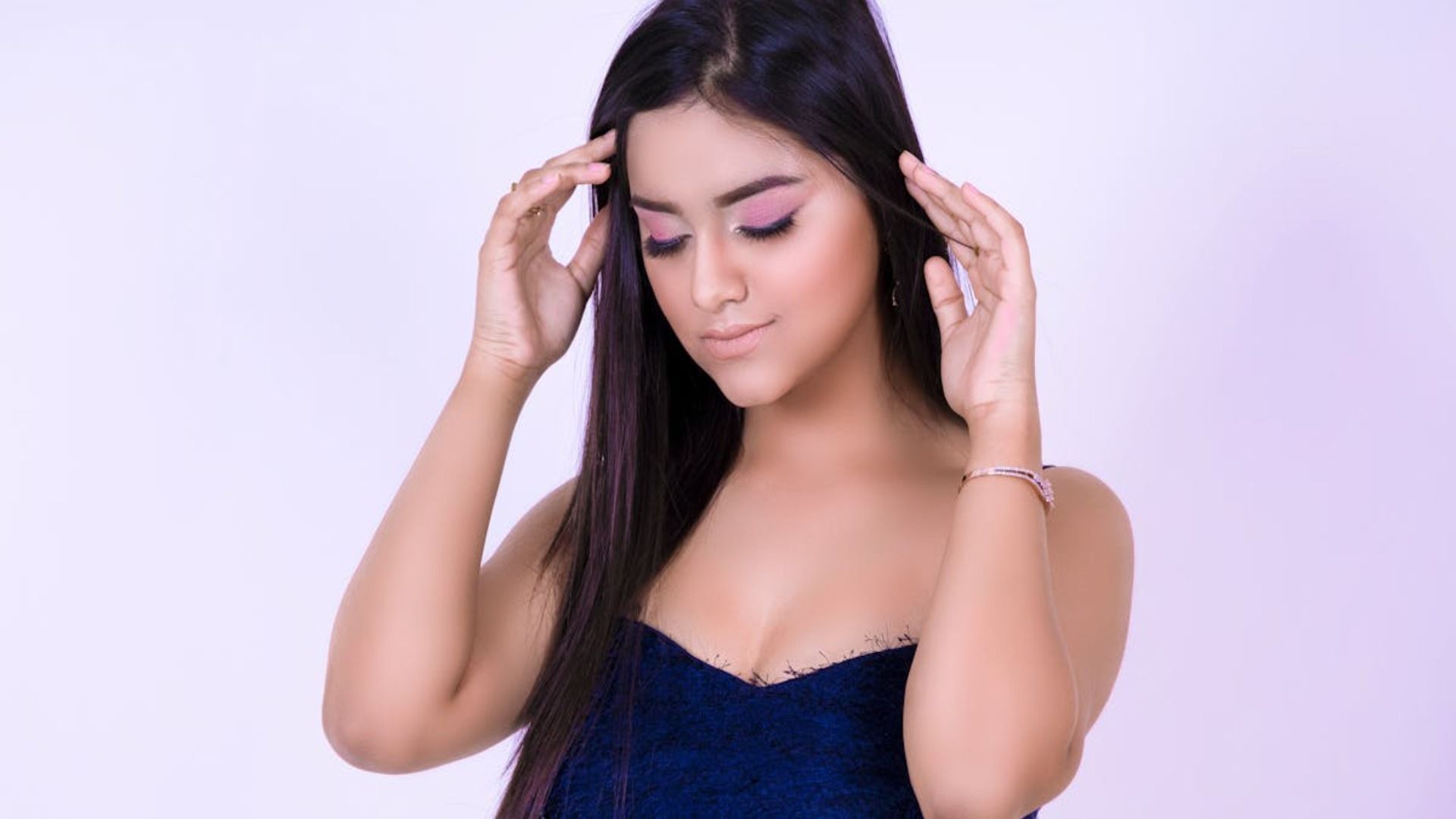 Una persona con un top oscuro sin tirantes posa contra un fondo claro con las manos levantadas