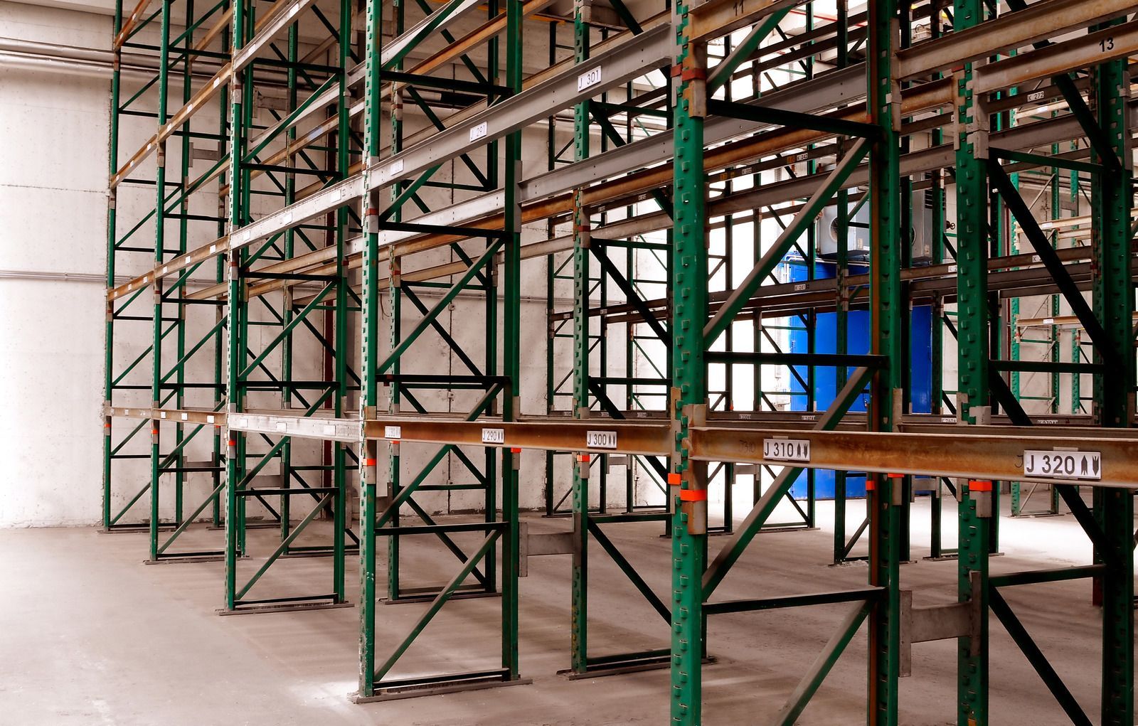 An empty warehouse with green shelves and a blue box in the middle.