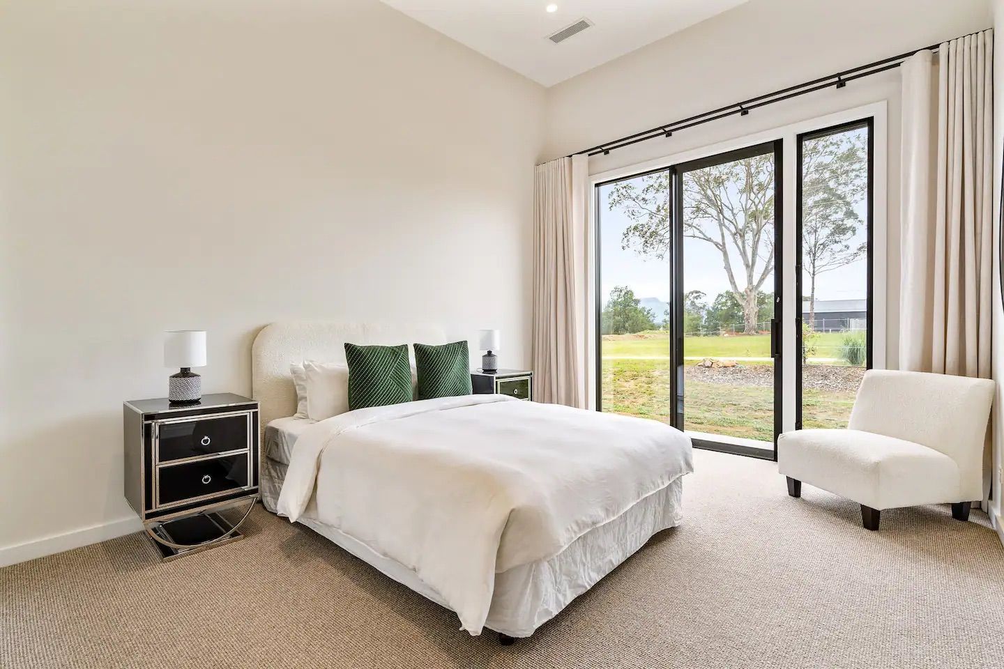 A bedroom with a bed , chair , nightstand and sliding glass doors.