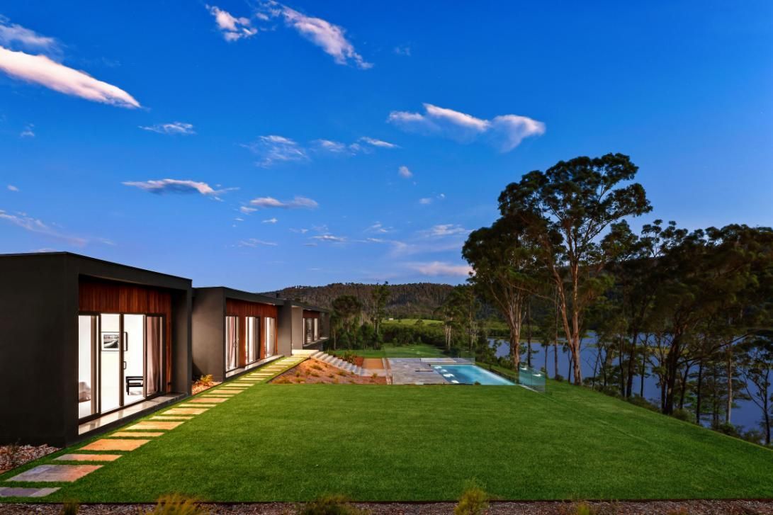 House Is Sitting On Top Of A Grassy Hill Next To A Body Of Water  — That Painter Guy In South Nowra, NSW