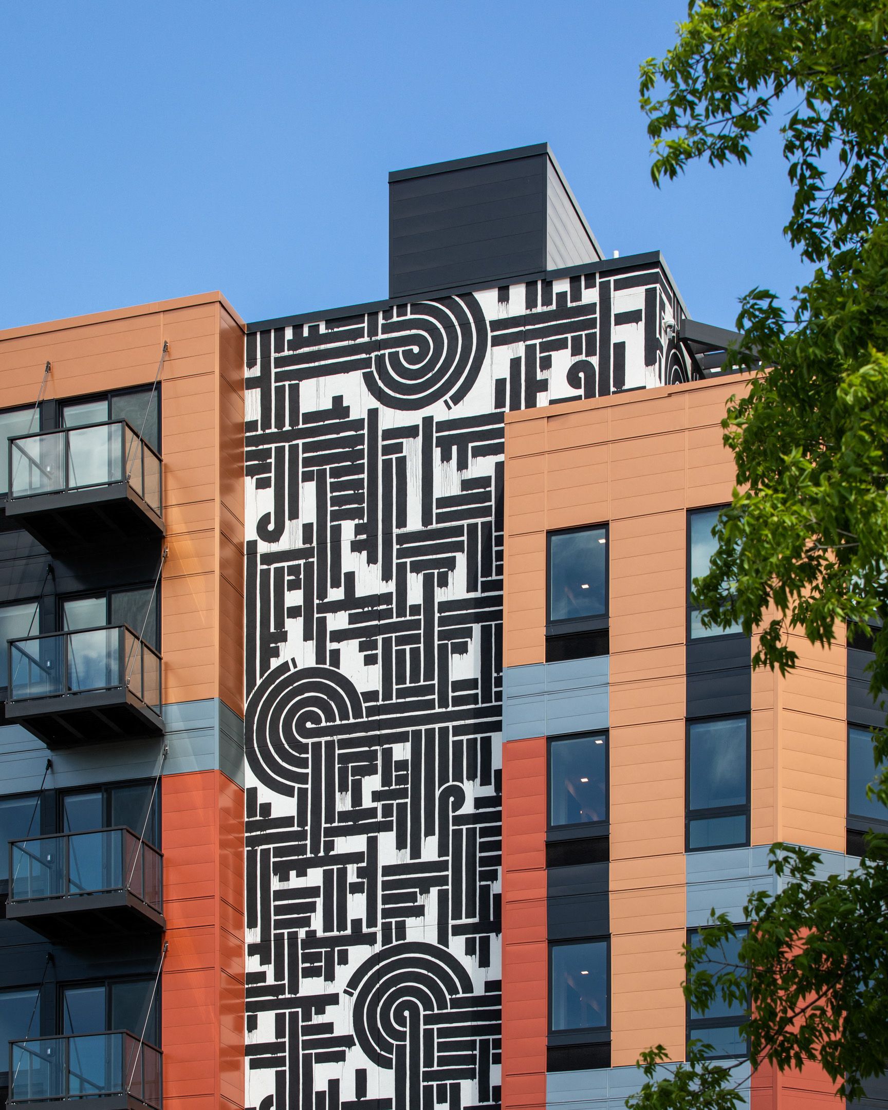 Exterior view of a modern apartment building with a large black-and-white geometric mural on the facade.