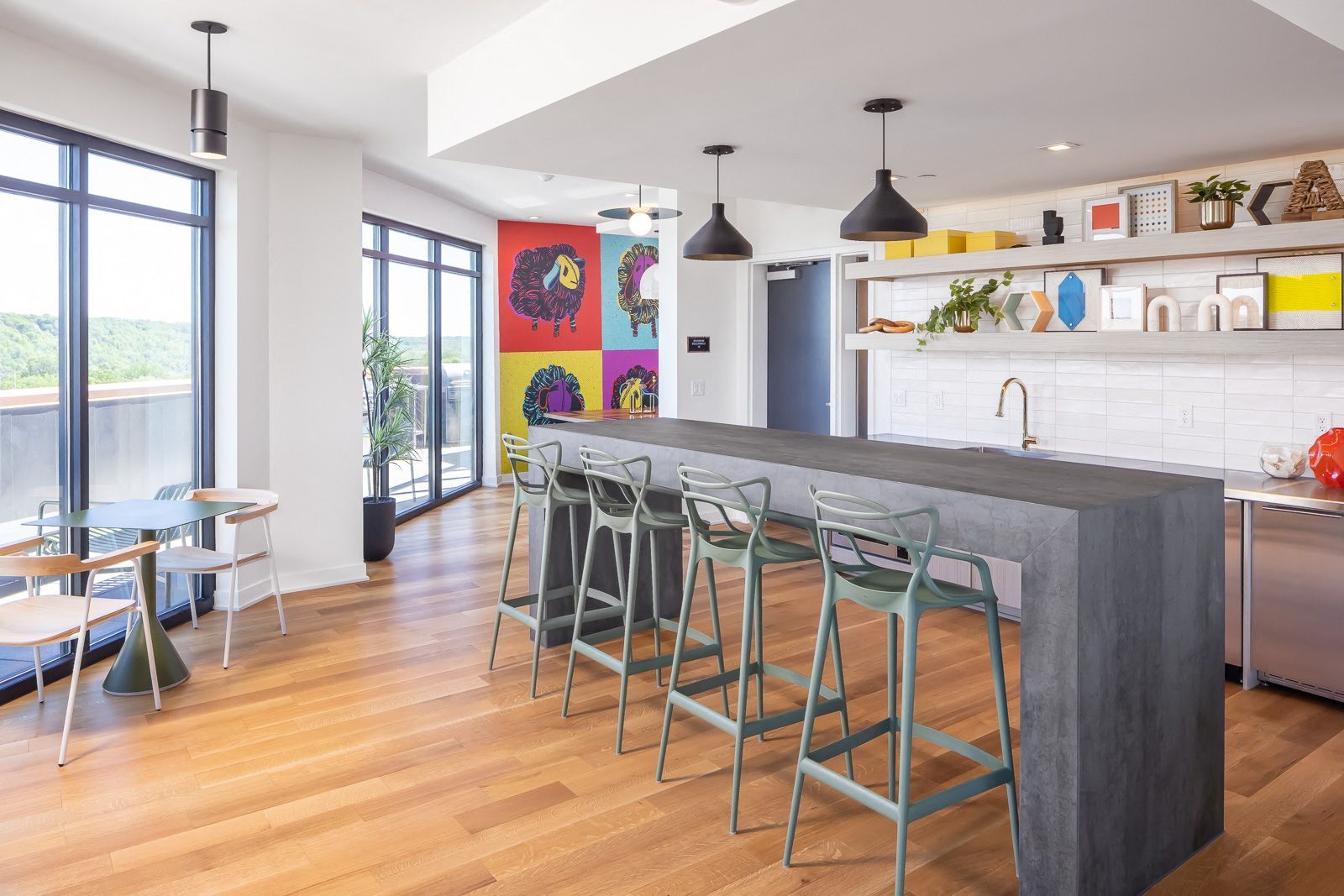 Bright communal kitchen and lounge with a large island, bar stools, art, and floor-to-ceiling windows.