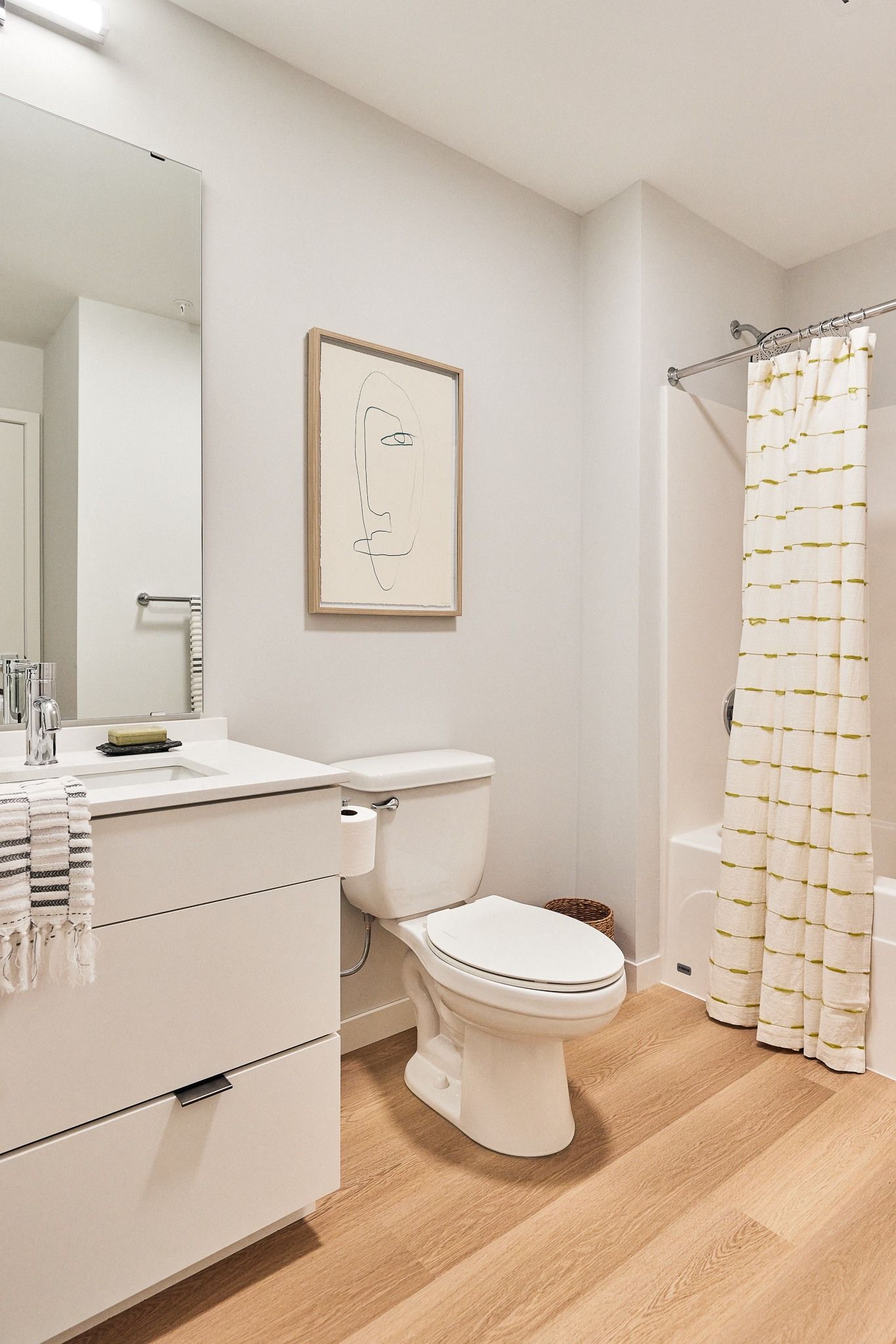 Modern bathroom with white vanity, toilet, and a striped white shower curtain.