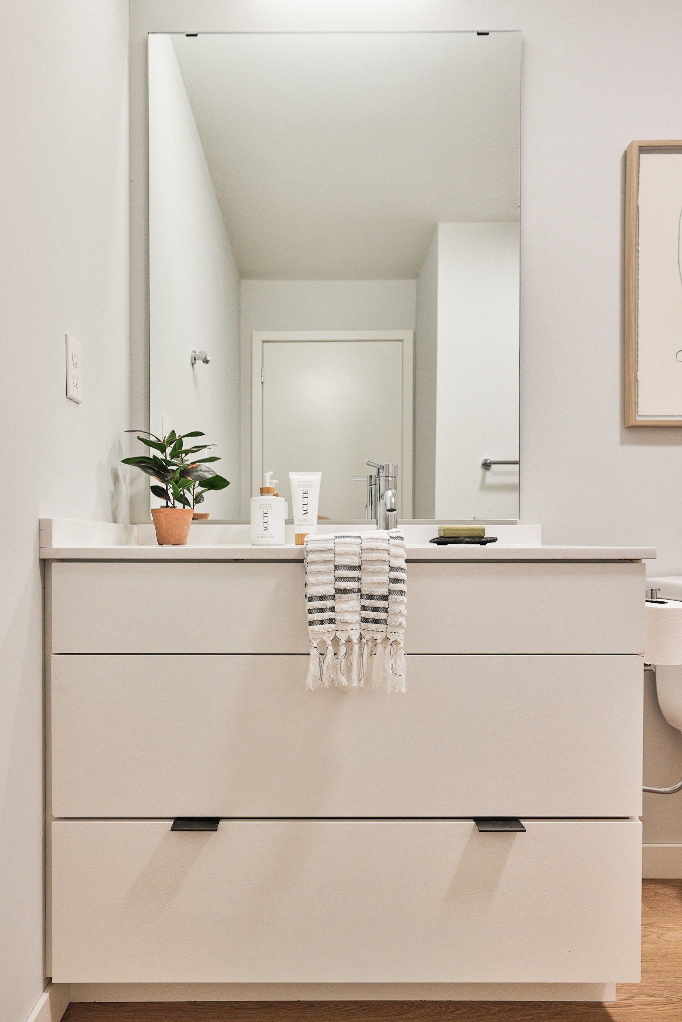 Modern bathroom vanity with large mirror, white cabinets, and a small potted plant.