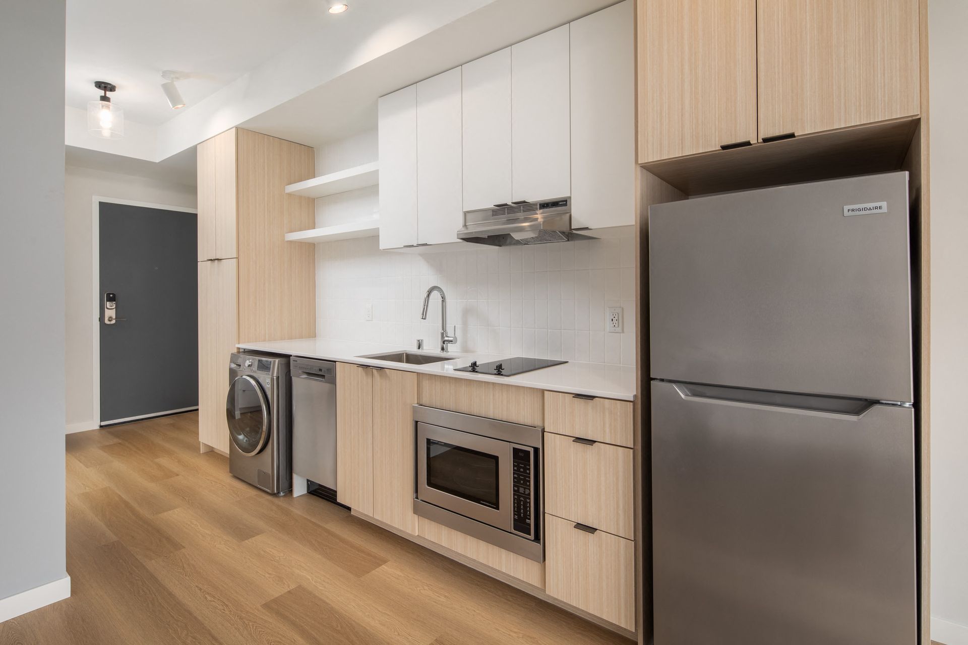 Modern apartment kitchen with stainless steel appliances, light wood cabinetry, and a white tile backsplash.