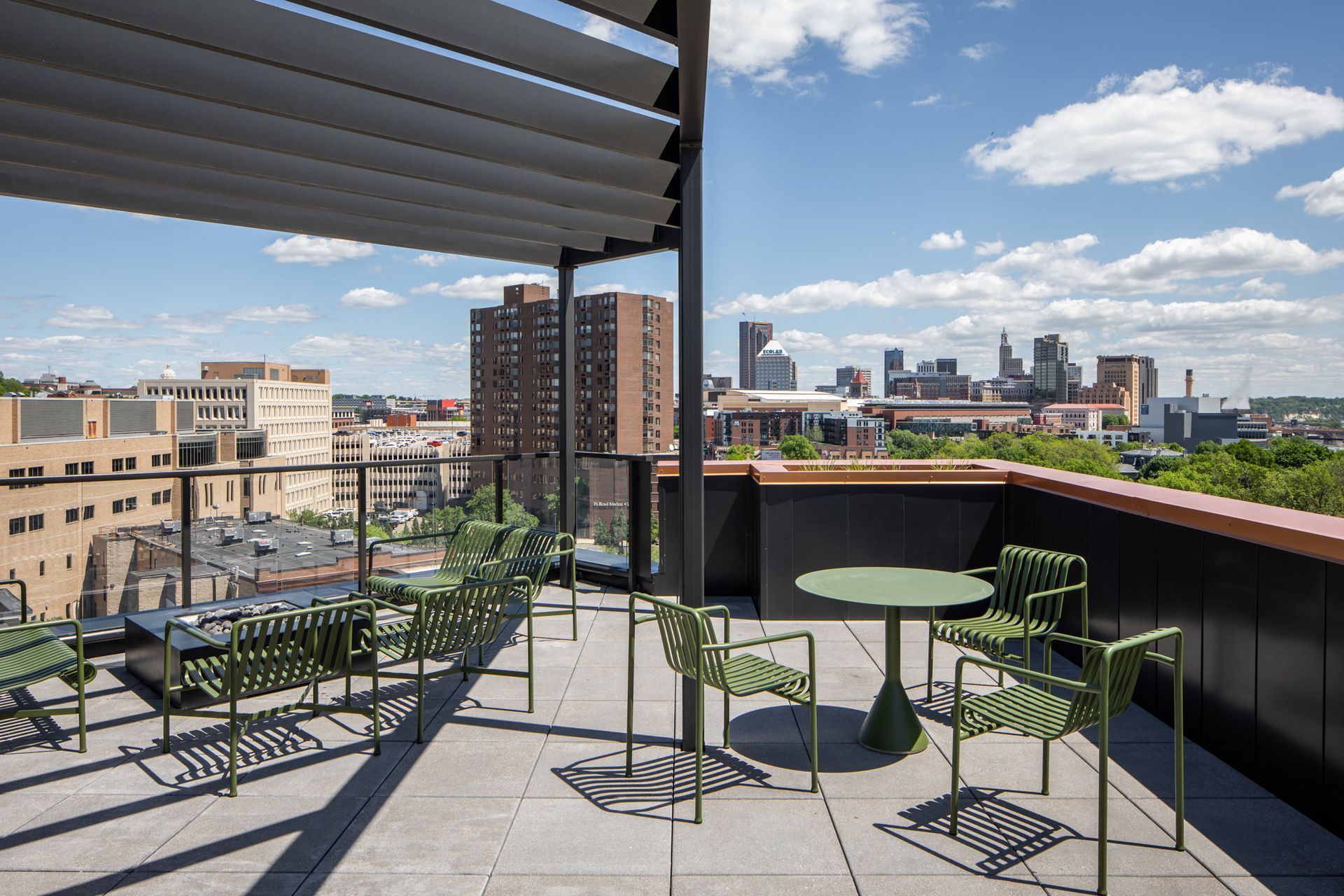 Rooftop terrace with green chairs and a round table, overlooking the city skyline.