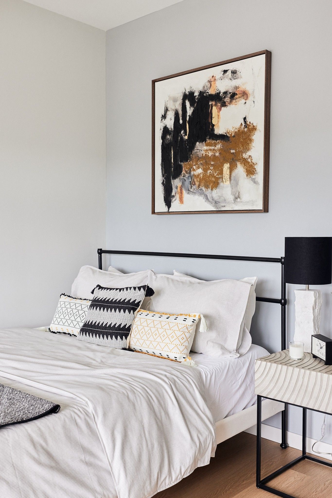 Bedroom with white bedding, black metal bed frame, and abstract wall art.
